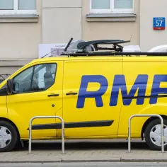 Żółty van RMF FM z niebieskim logo na tle budynku.
